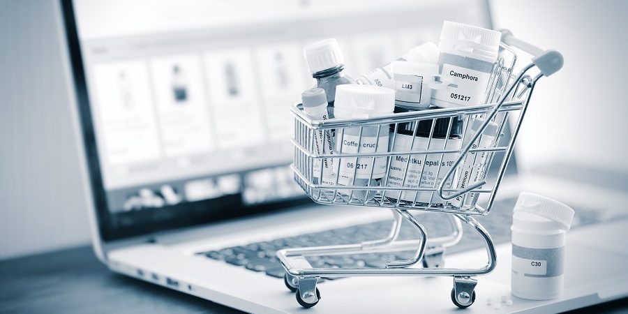 Mini shopping cart full of homeopathic remedies on laptop background. Homeopathy and internet online shopping concept.